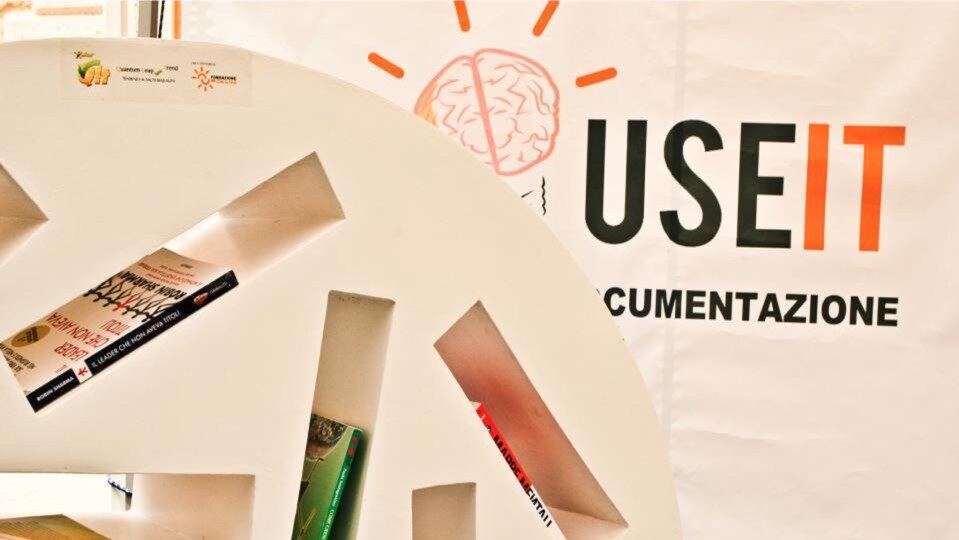 Scaffalatura e angolo di lettura del centro USE IT, con banner e logo