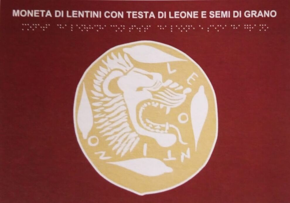 Moneta di Lentini con testa di leone e semi di grano, con trascrizione in braille
