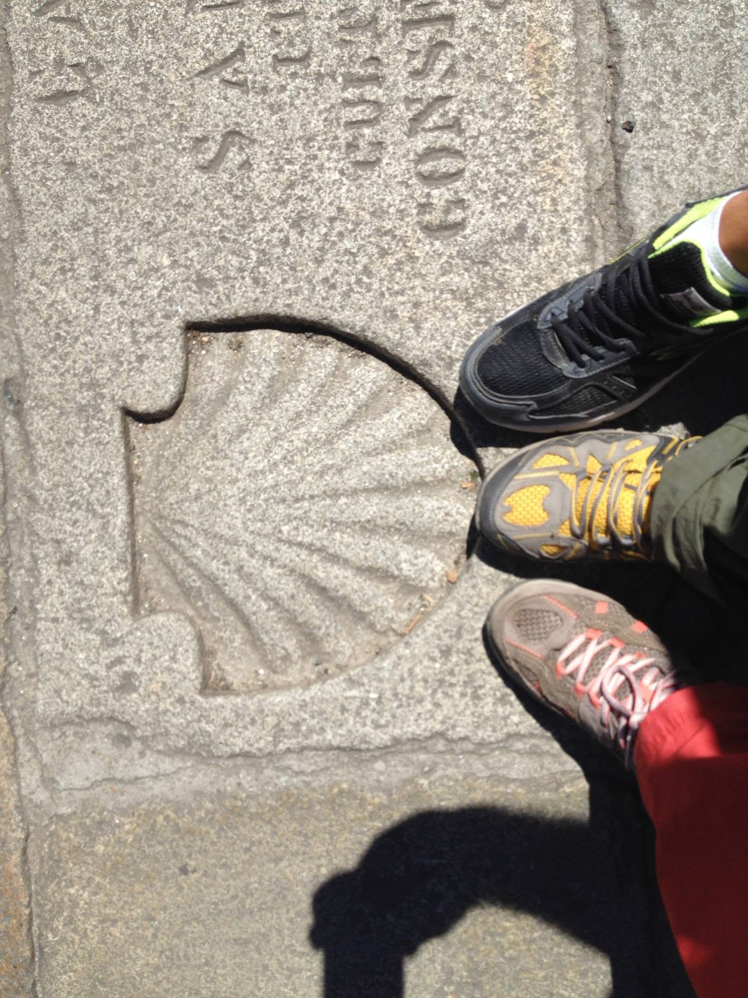 Scarponi da trekking di un gruppo di pellegrini su una pietra miliare incisa del Camino de Santiago