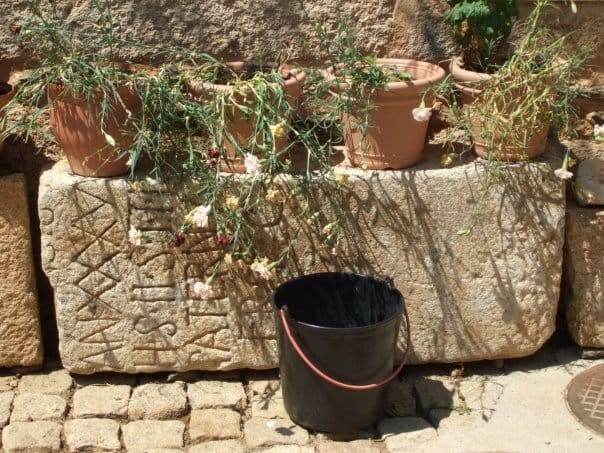Iscrizione lapidea antica con vasi di fiori e un secchio, in Portogallo